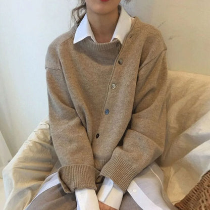 Beige cardigan med asymmetrisk knaplukning og ribstrikkede kanter, rund hals.