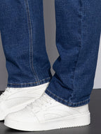 Blå jeans med lige ben og rå kant ved anklen, hvide sneakers synlige