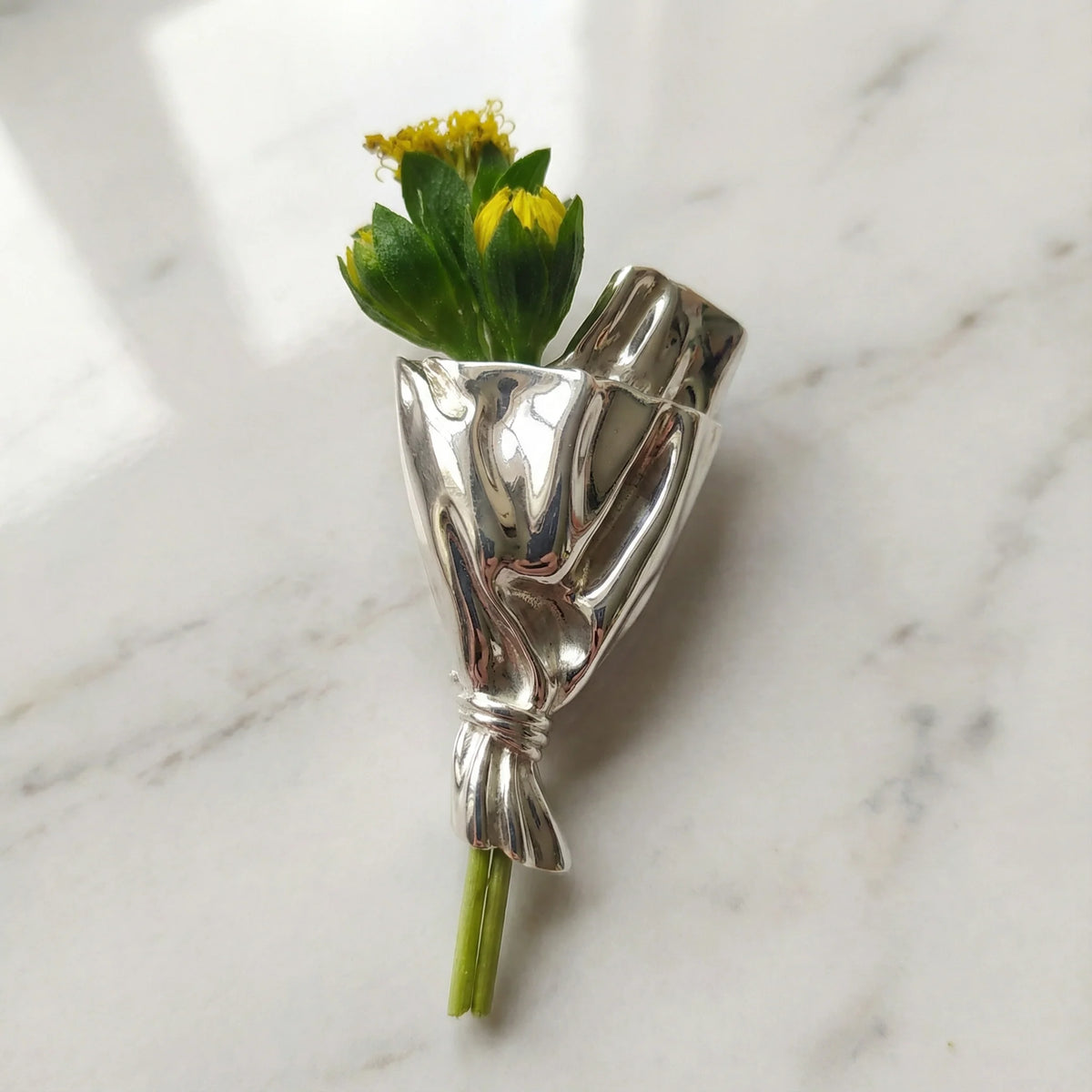 Blomsterbuket-broche i sølv med små blomster samlet i metalbuket udenfor.