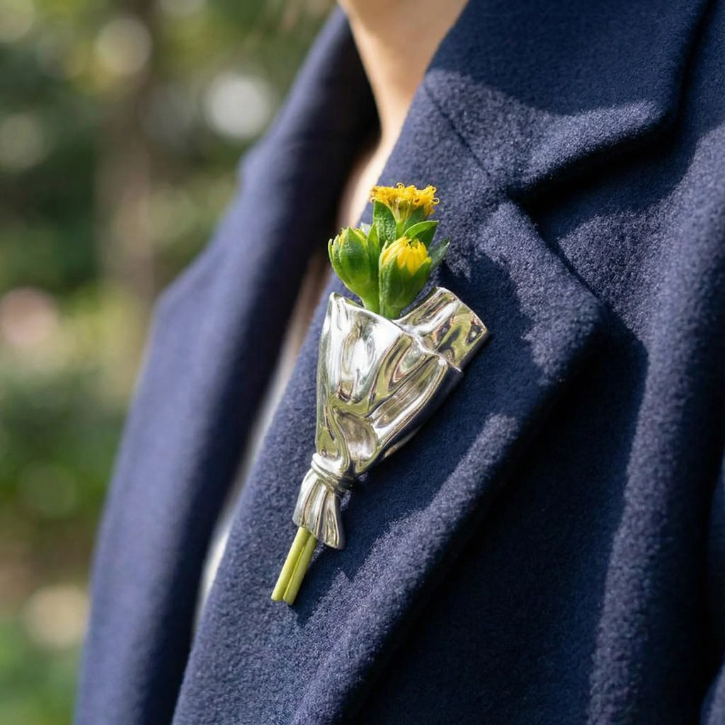 Blomsterbuket-broche i sølv med gul-grøn buket prydet på mørkt tøj.
