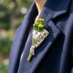 Blomsterbuket-broche i sølv med gul-grøn buket prydet på mørkt tøj.