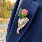 Blomsterbuket-broche i guld med lyserød blomst og grønne blade monteret på tøj.